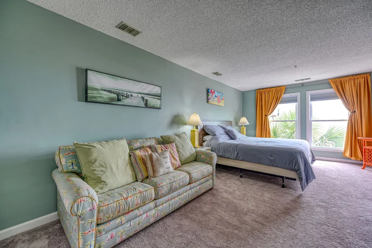 A welcoming suite layout with a sofa and bed positioned near large windows, complemented by tasteful artwork on the walls. Natural light streams into the room, enhancing the comfortable and communal ambiance ideal for both relaxation and flexible sleeping arrangements.