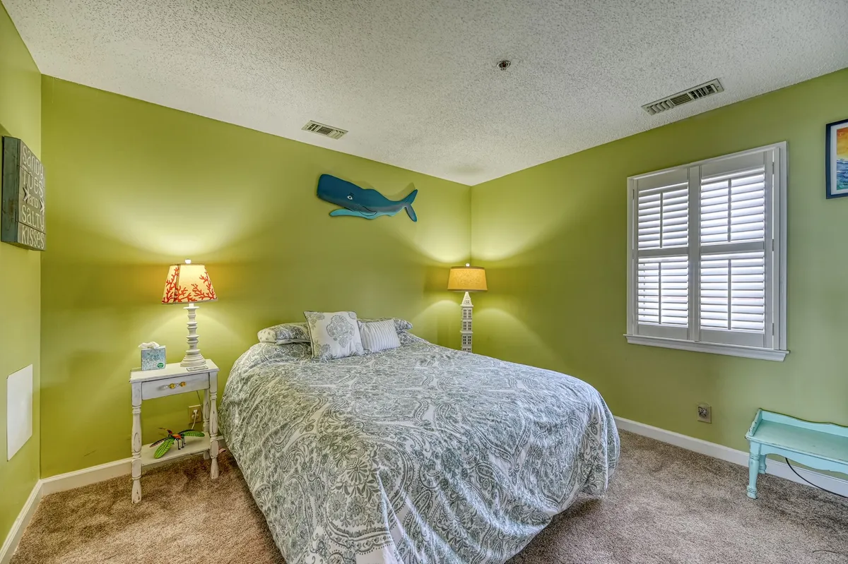 A tranquil bedroom with patterned bedding, charming whale wall art, a nightstand with a lamp, and a shuttered window. The room is cozy and bright, ideal for quiet moments and restful sleep.
