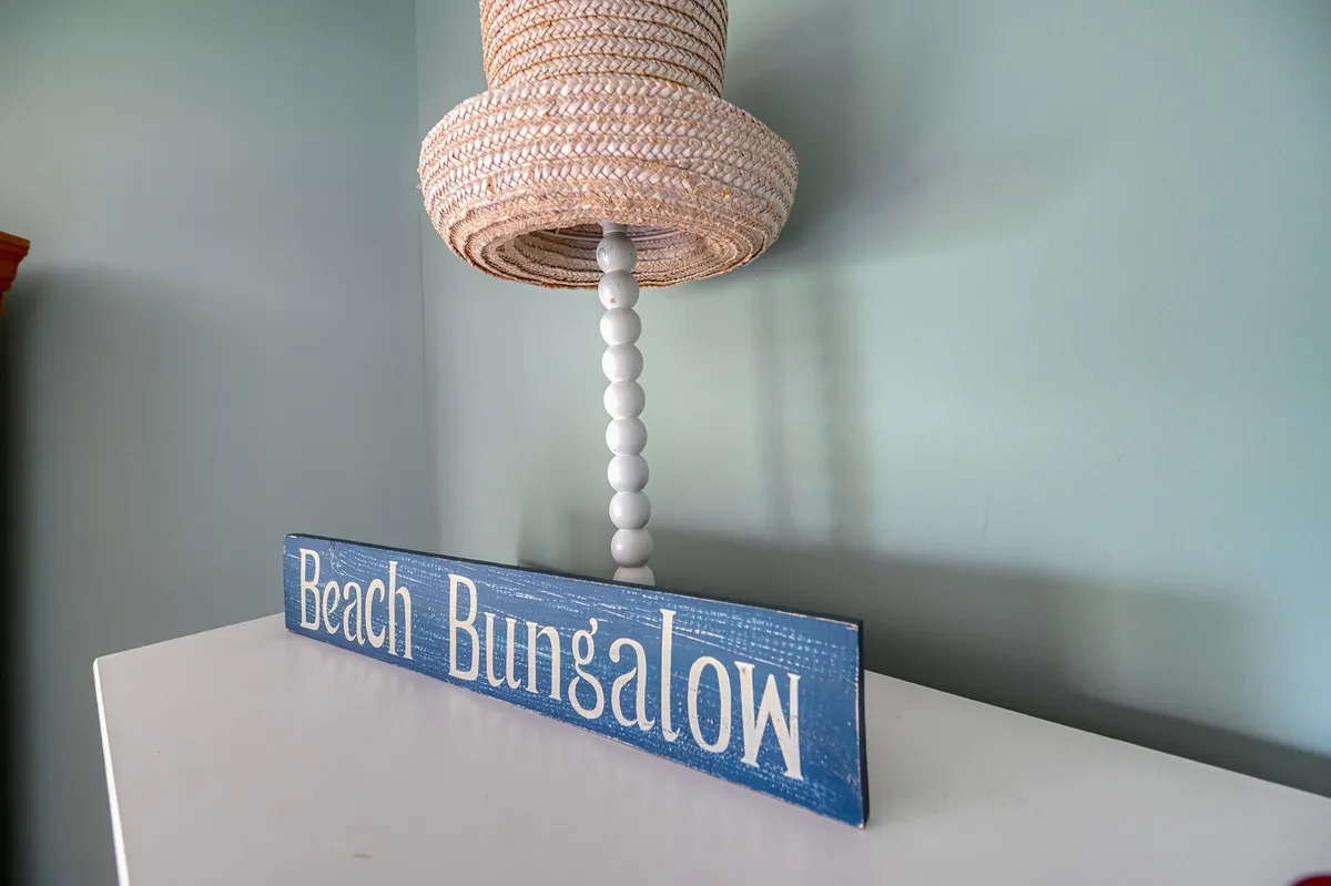 This image features a 'Beach Bungalow' sign paired with a woven lamp shade, subtly suggesting proximity to the coast and evoking a relaxed, beachy vibe. The decor hints at sunset views and the ease of transitioning from indoor comfort to outdoor adventures.