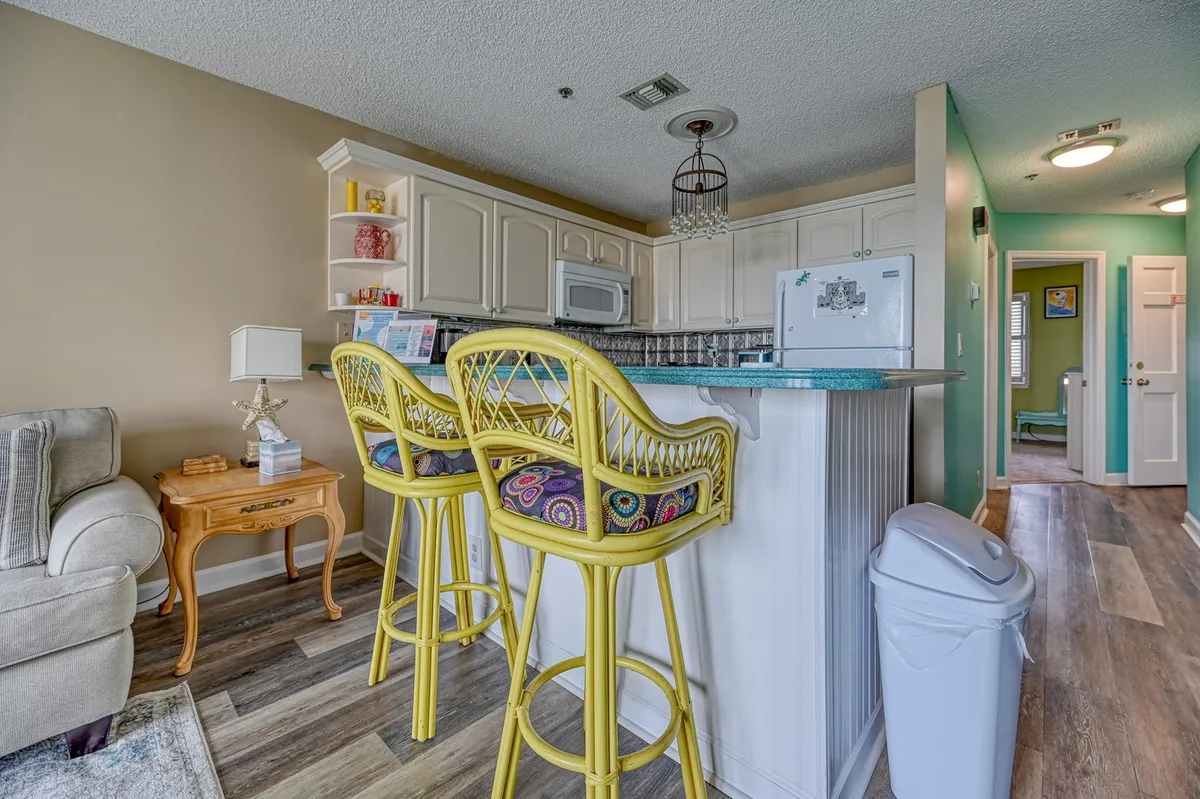 Showcasing a cheerful and functional kitchen space, the image includes a kitchen island with yellow bar stools, decorative shelving, and homey touches. The layout invites guests to gather, cook, and dine together in comfort.